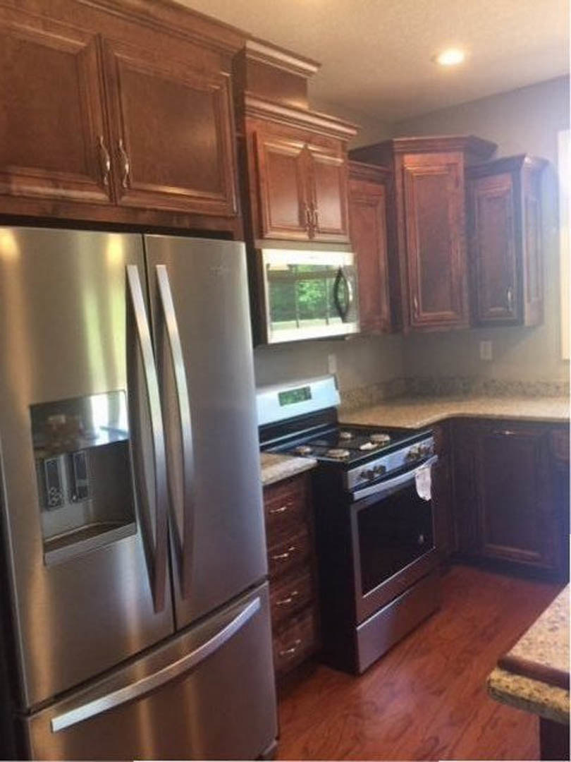 Modern kitchen featuring stainless steel refrigerator and stove, white cabinetry, stone countertops, and a window with metal handle