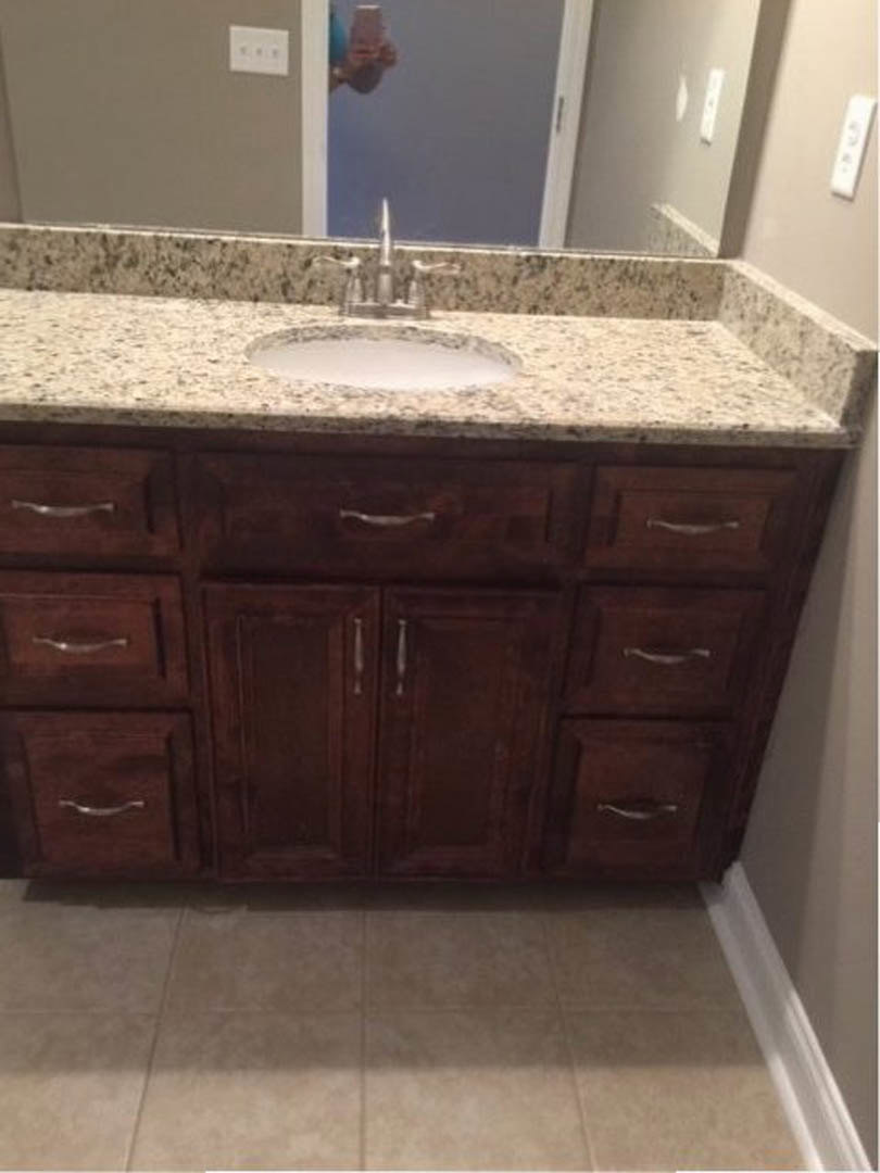 Marble bathroom countertop with undermount sink, chrome faucet, large framed mirror, white wall outlet with black switches, light tile flooring, white cabinetry drawers