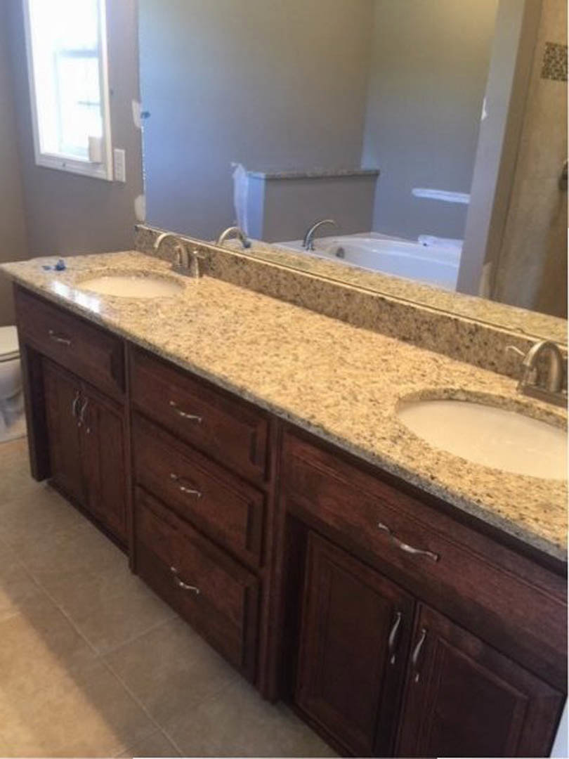 Bathroom with expansive wall mirror above double sinks, white quartz countertop, chrome faucets, light wood cabinetry, and neutral tile backsplash