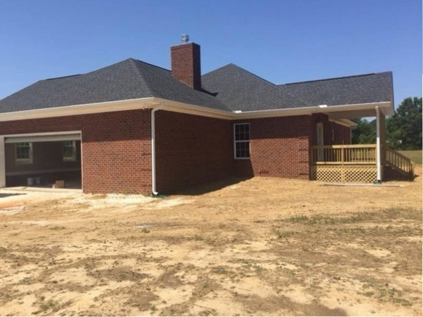 Red brick house with white trim, covered porch, wooden lattice fence, chimney, and white-framed windows; dirt yard in foreground
