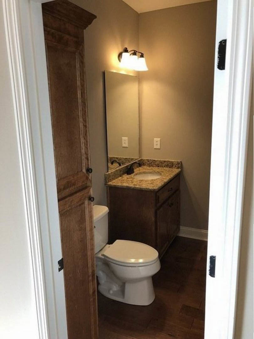 White porcelain sink with chrome faucet beside toilet, beige tile flooring, wall-mounted mirror above sink, three-light fixture, neutral painted walls.