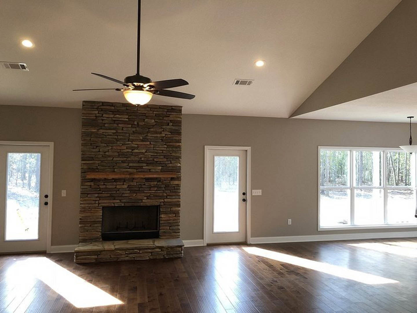 Living room with brick fireplace and wood mantel, ceiling fan with light, dark flooring, door with window overlooking forest