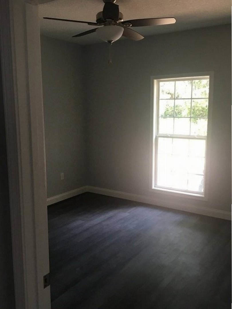 Bright room with white-framed window, ceiling fan with light, dark wood flooring, and smooth plaster walls