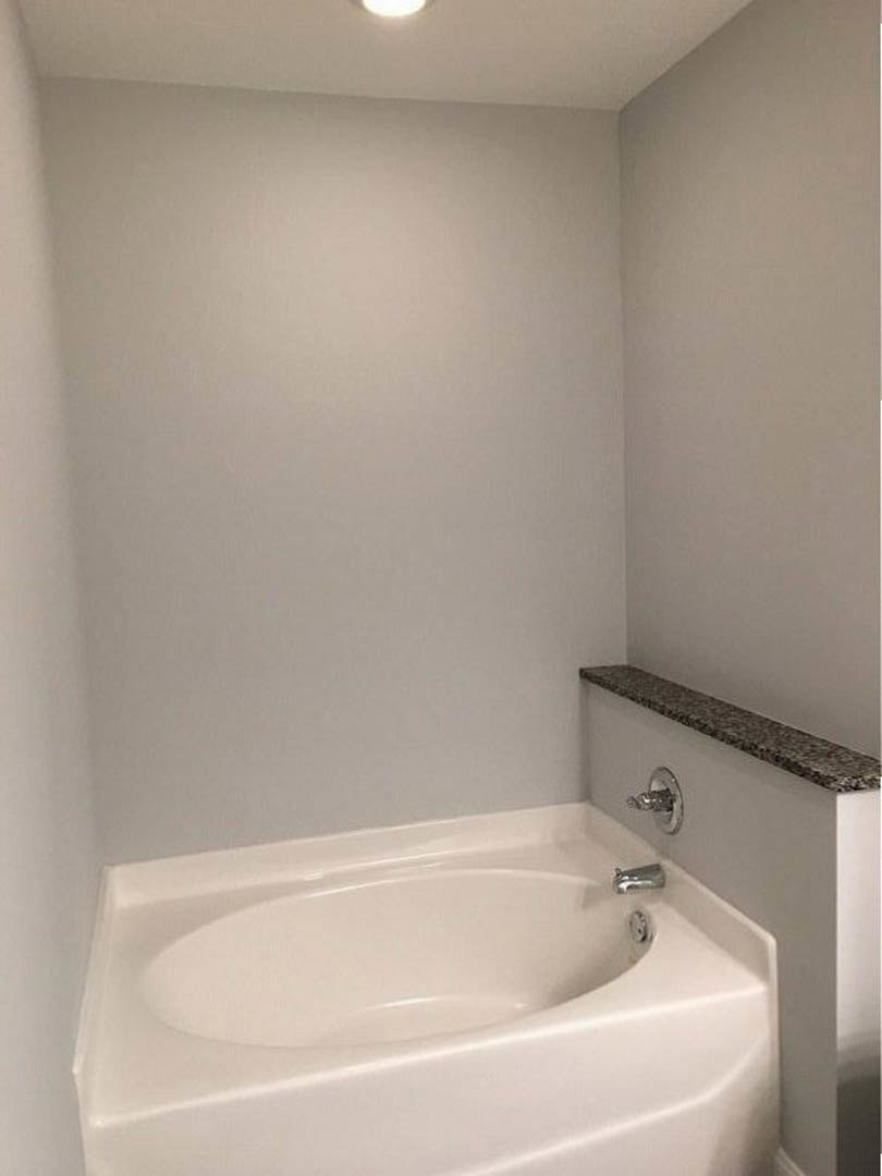 Freestanding white bathtub with curved edge set against tiled bathroom wall, chrome faucet, and nearby sink