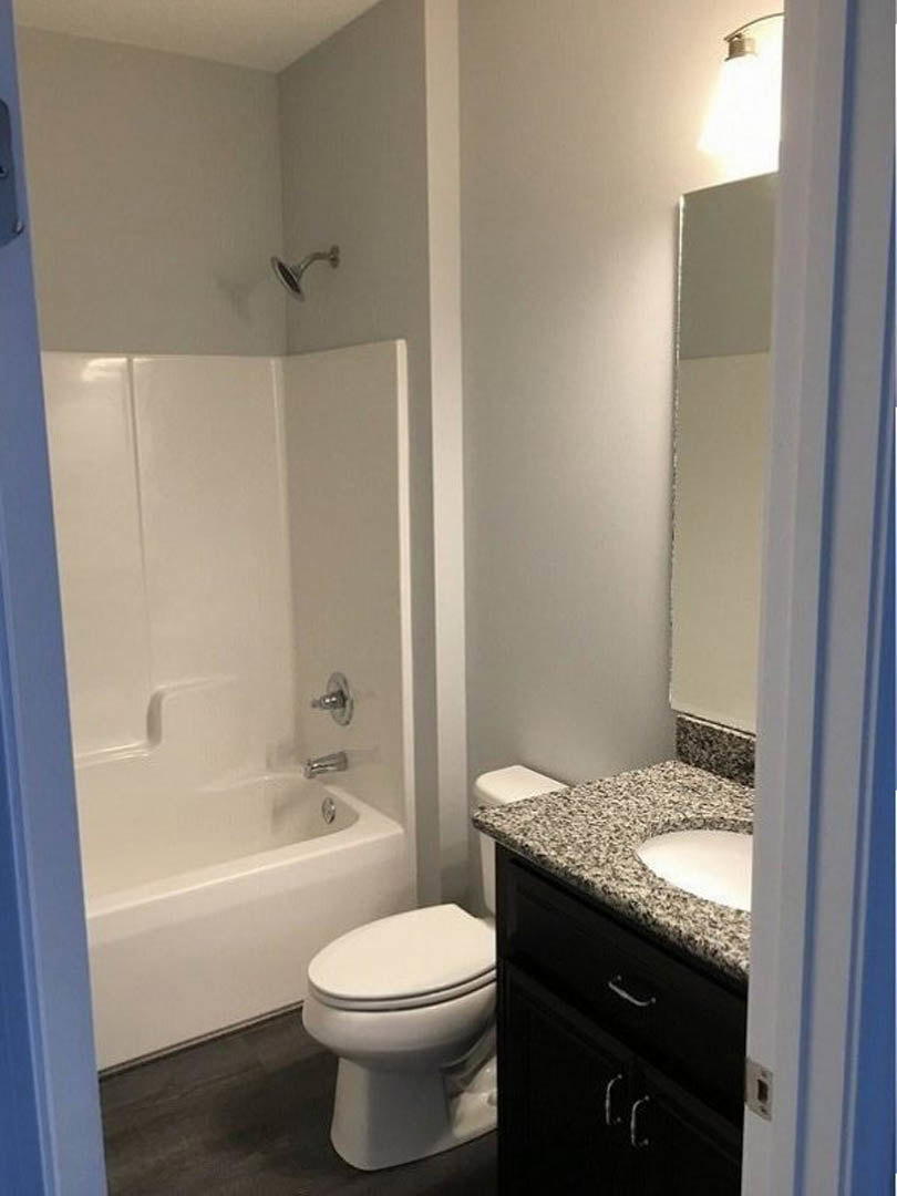 Modern bathroom with white ceramic sink, chrome faucet, wall-mounted mirror, and toilet; gray tile flooring and light-colored tiled walls