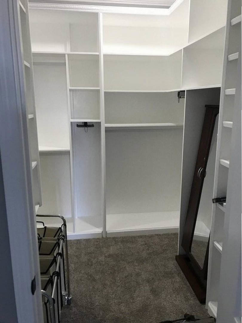 Walk-in closet with built-in white shelves, full-length mirror, and light wood flooring