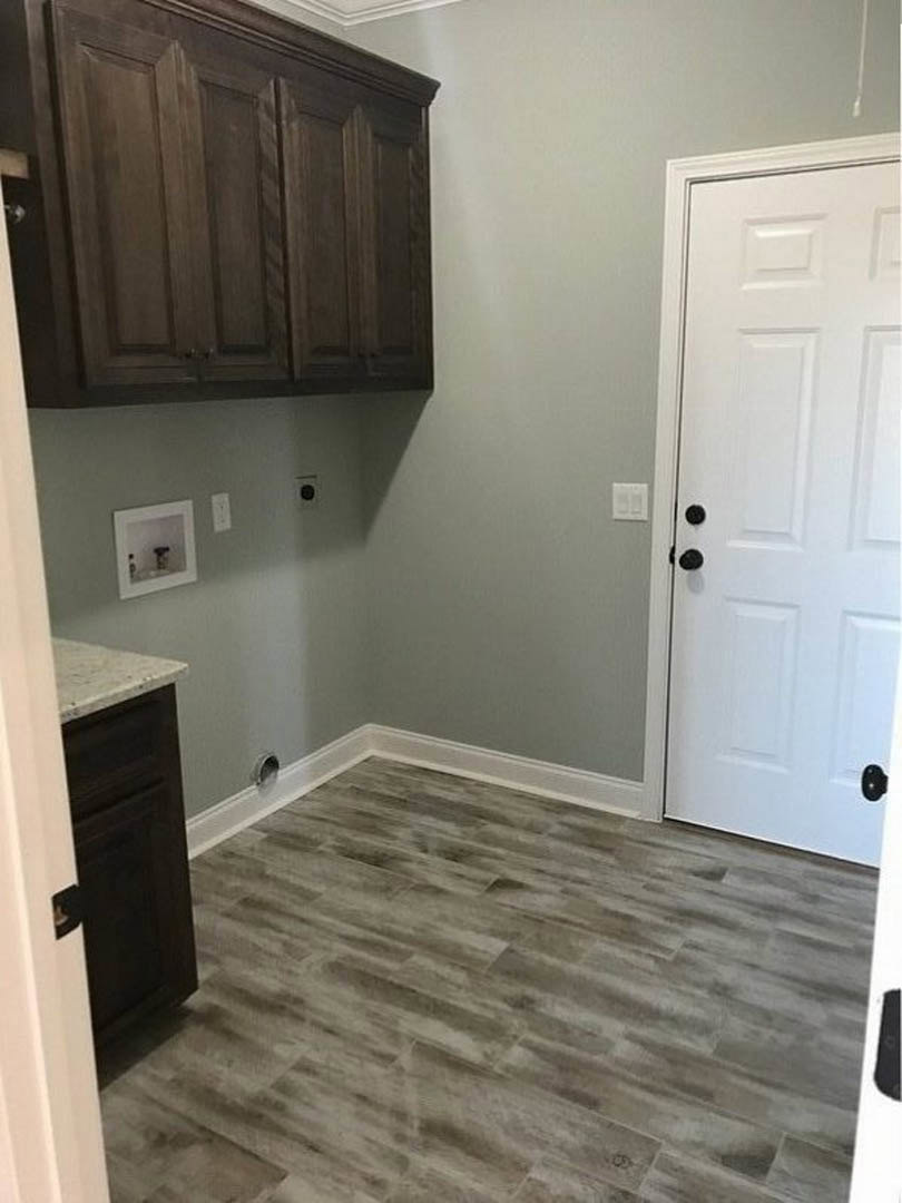 Wood cabinets with black knobs, wood flooring with white trim, white door, framed picture on wall