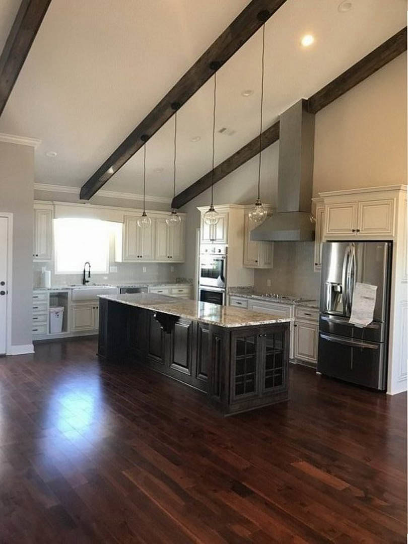 Kitchen with dark wood flooring, marble-topped island, white cabinetry, exposed ceiling beams with recessed lighting, stainless refrigerator with paper attached.