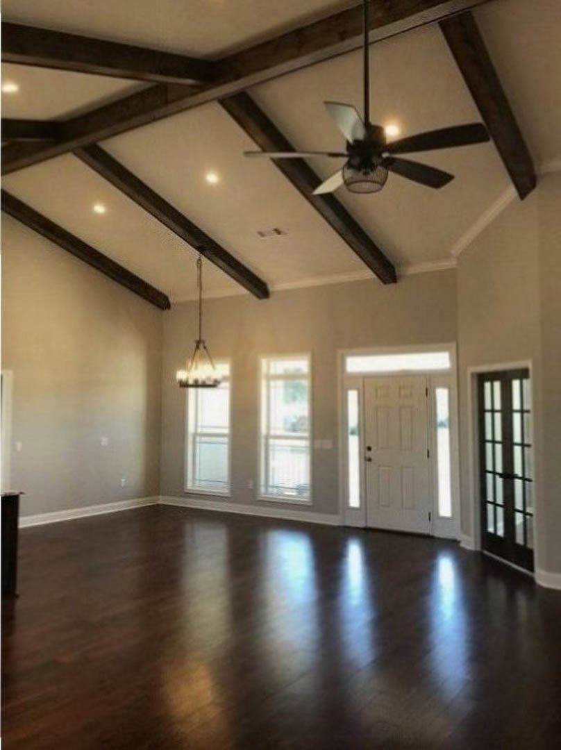 Dark hardwood floors, white paneled door with glass inserts, ceiling fan mounted on white ceiling, large window allowing daylight into neutral-toned room