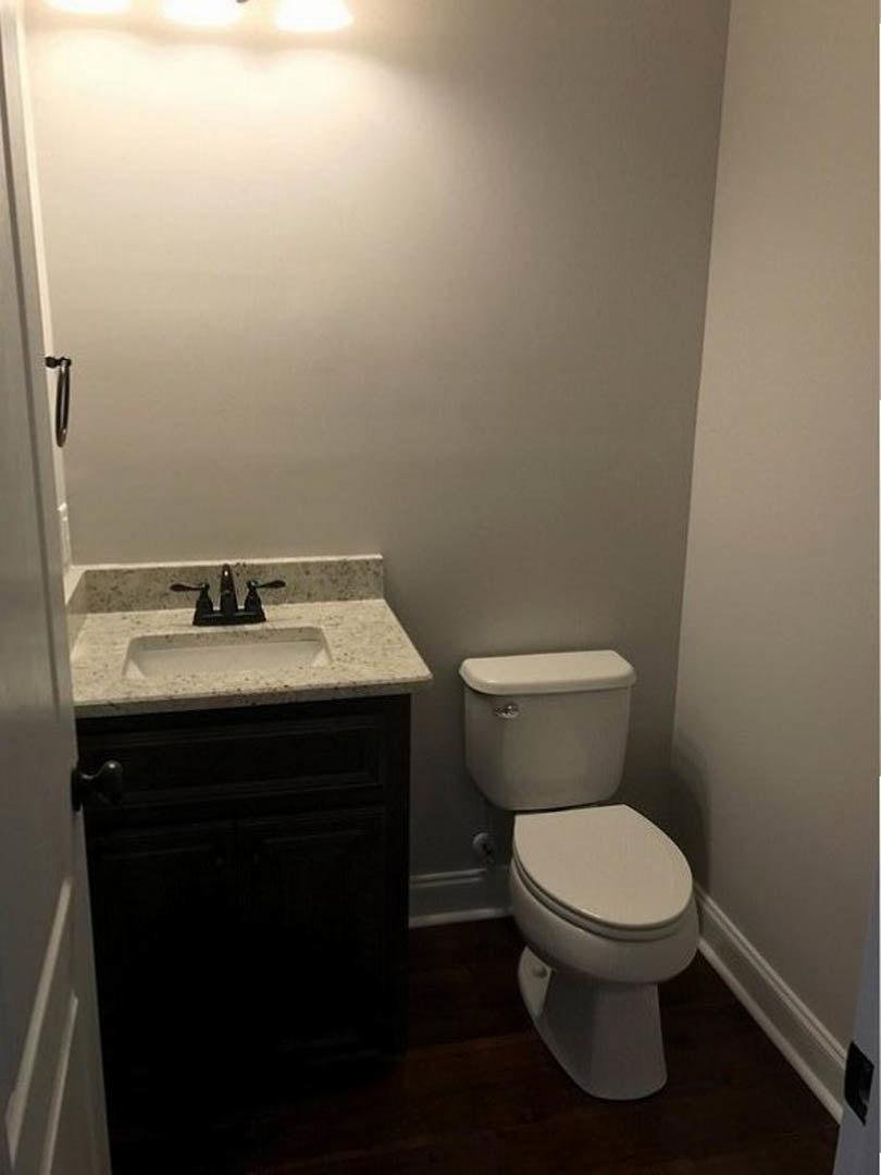 White porcelain toilet with closed lid, rectangular sink with chrome faucet, light-colored tile walls, and silver toilet handle in a modern bathroom.