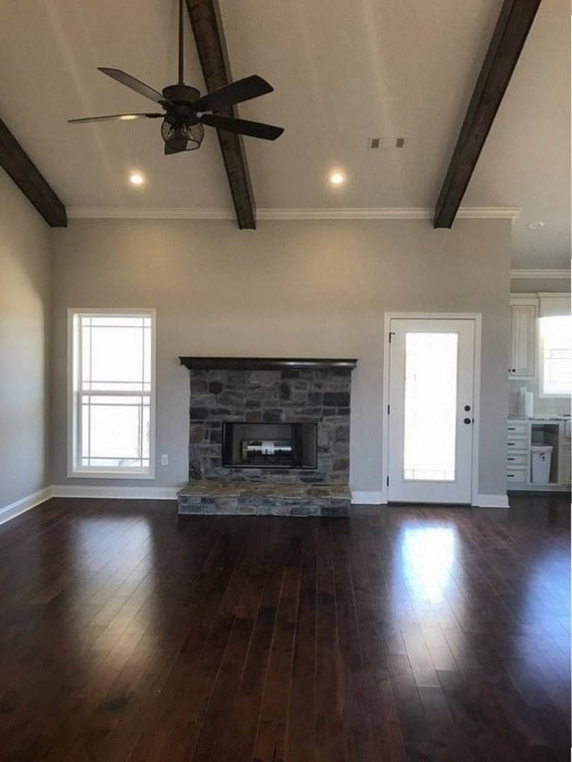 Living room with hardwood floors, stone fireplace, black hearth, ceiling fan, and white-framed window