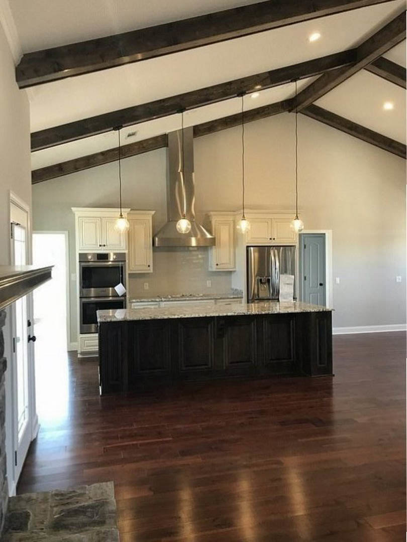 Spacious kitchen featuring a large marble-topped island, stainless steel refrigerator, built-in microwave, white cabinetry, and hardwood flooring.