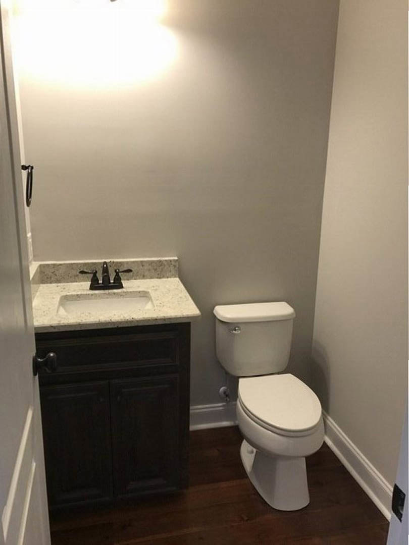Modern bathroom with white toilet, rectangular sink, gray tile walls, and concrete step flooring