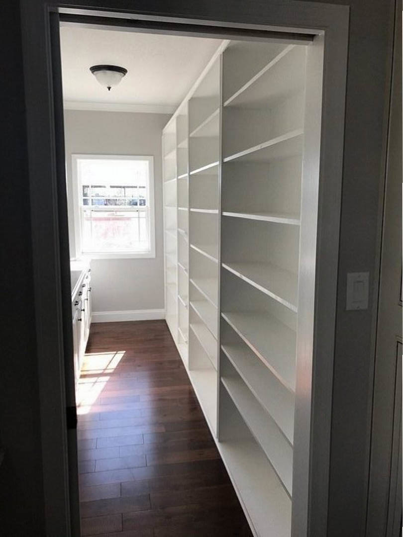 Dark wood floor with built-in white shelves along the wall, white-framed window, recessed lighting, and a white rectangular accent object in a modern room
