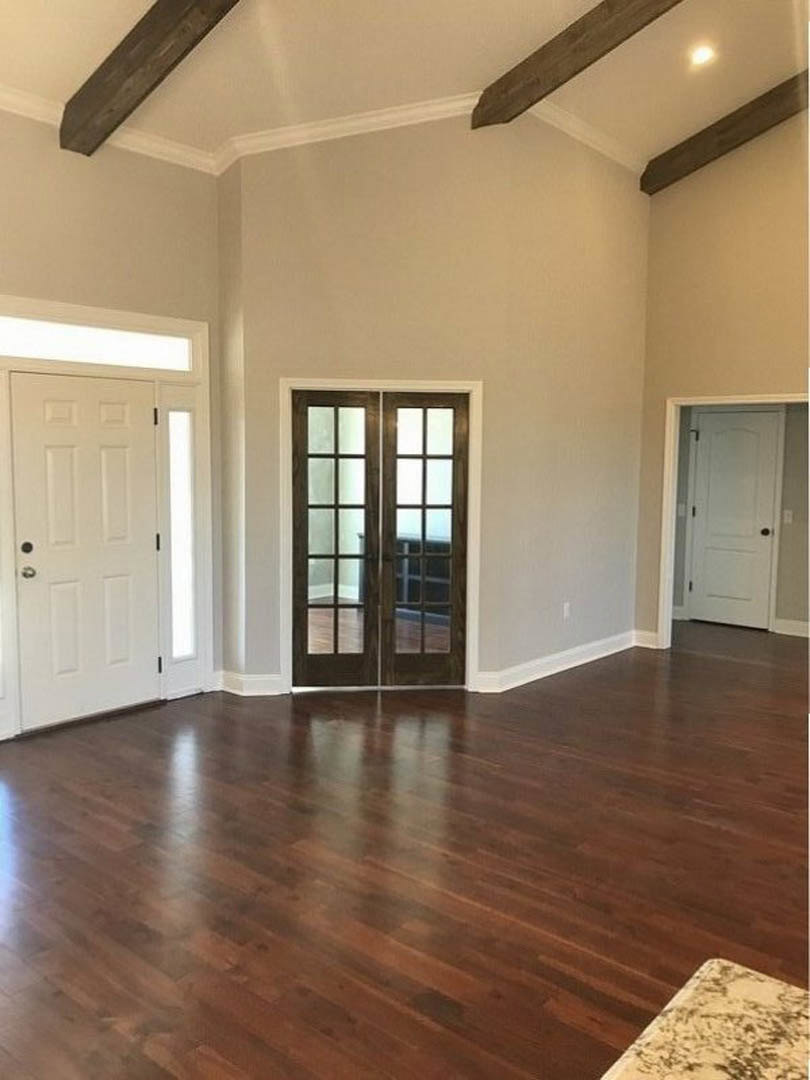 Hardwood floor room with white double doors featuring glass panes, black hardware, and light walls
