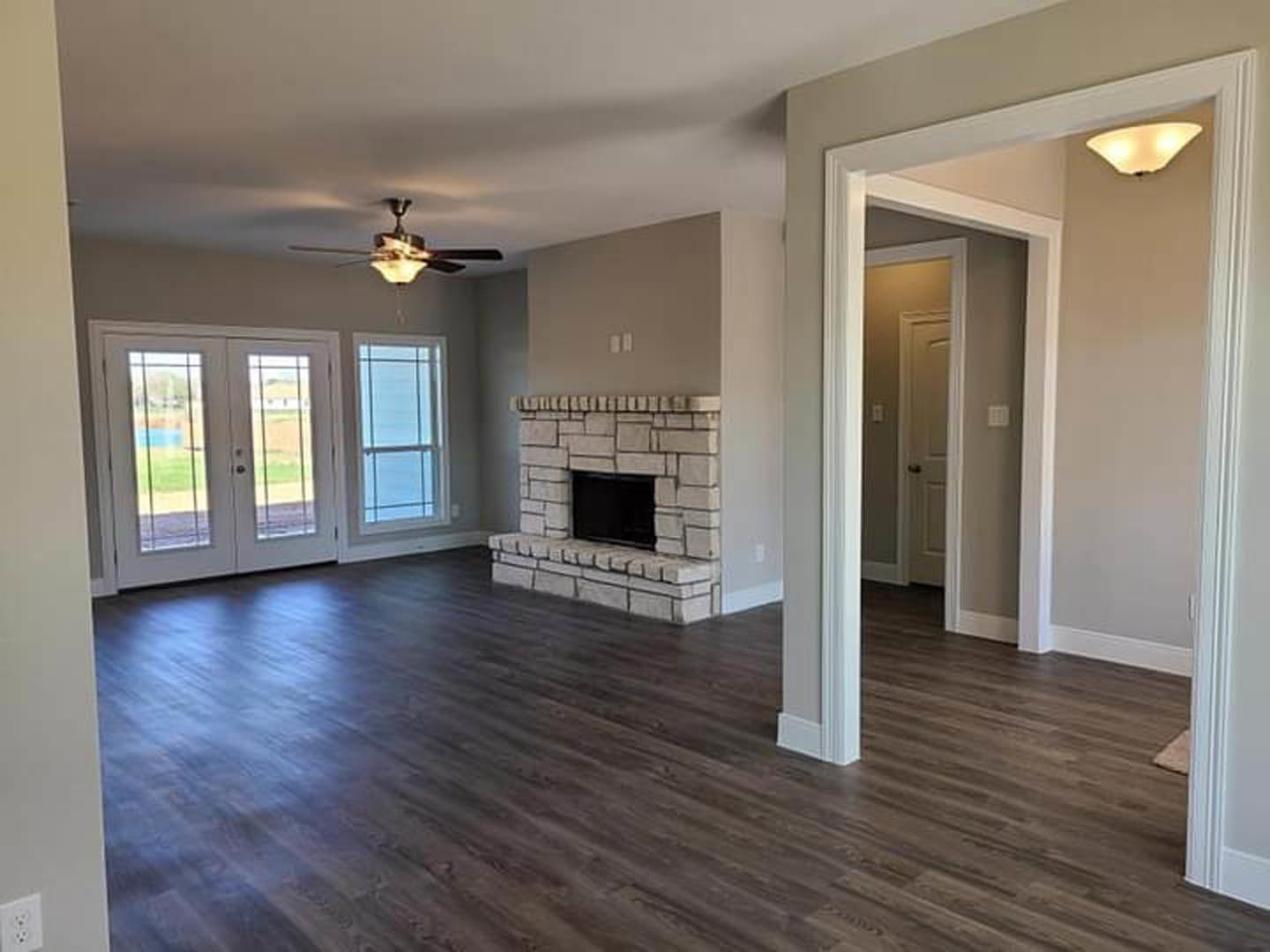 Living room with hardwood floors, brick fireplace featuring a black screen, ceiling fan with light, and double glass-paneled doors