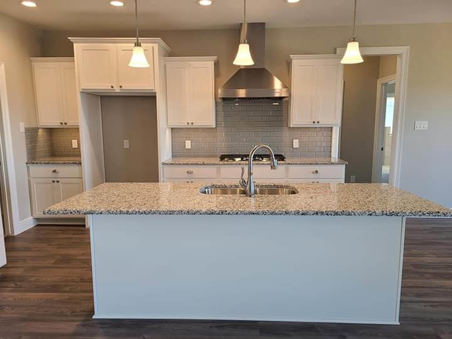 Granite kitchen island with undermount sink, stainless steel faucet, white cabinetry, tile backsplash, and stainless steel range hood