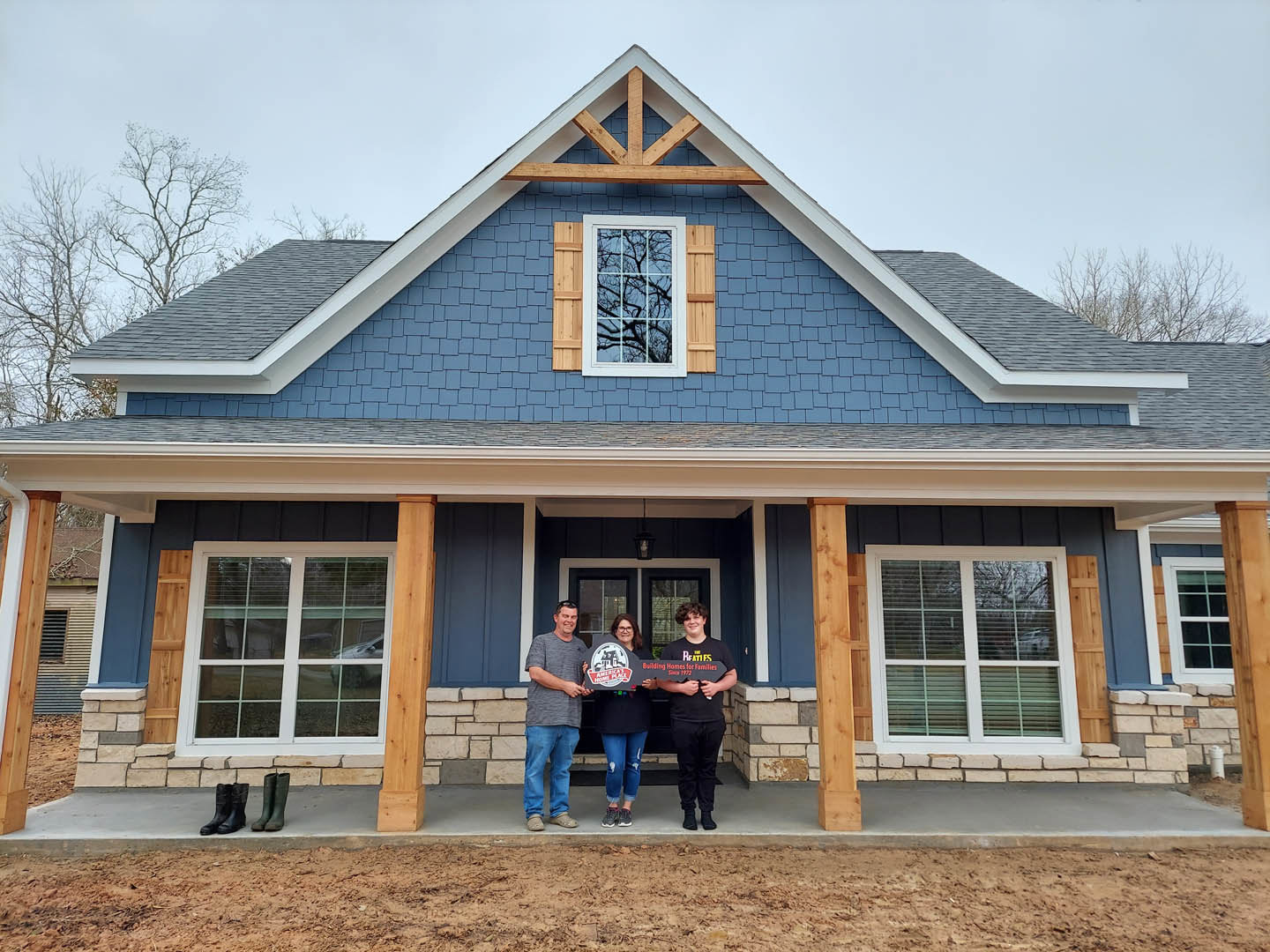 Group of people holding signs in front of a modern home with white siding, sash windows reflecting trees, and a grey roof