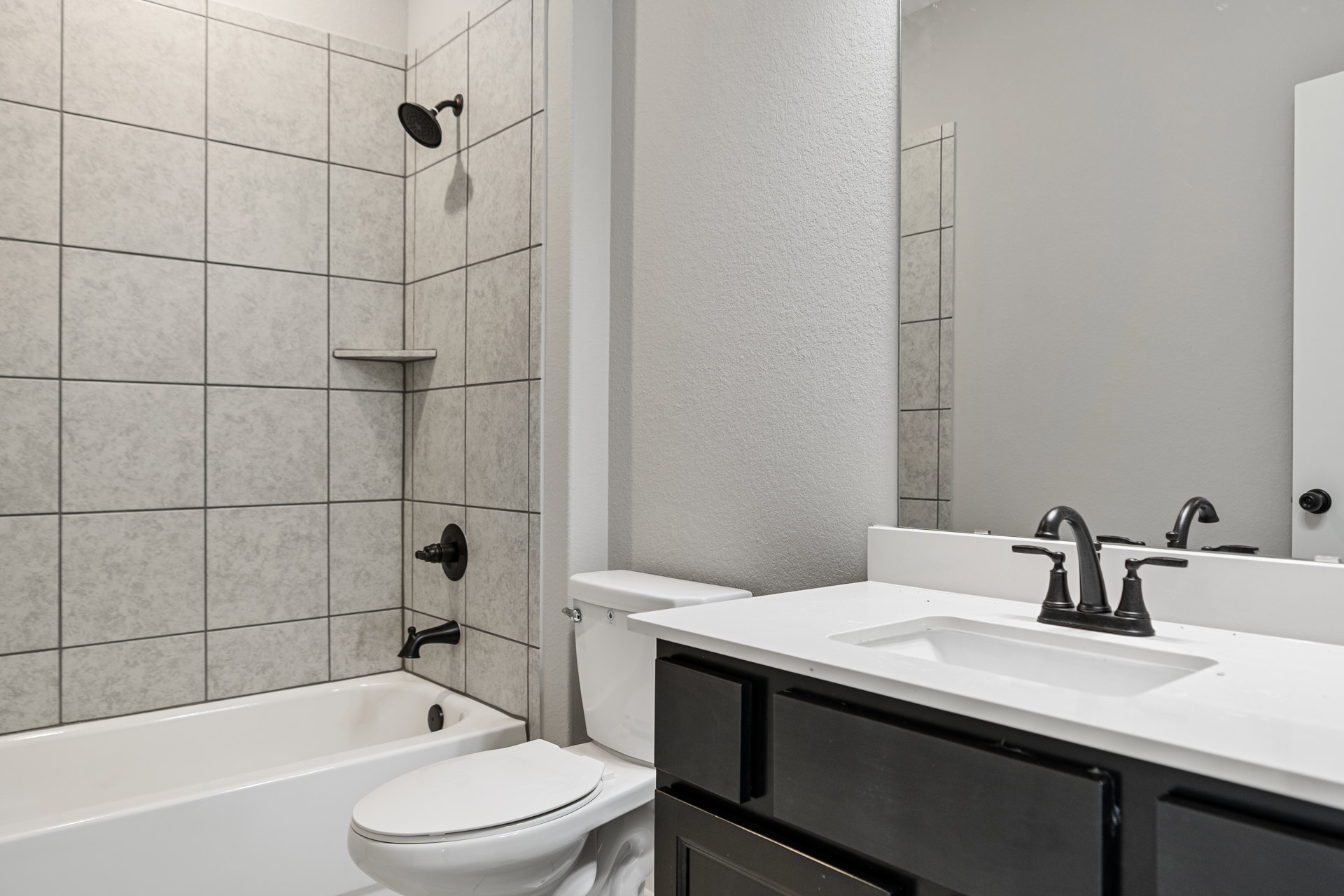 Modern bathroom with white porcelain sink, chrome faucet, white toilet with closed lid, tiled walls, and black countertop border