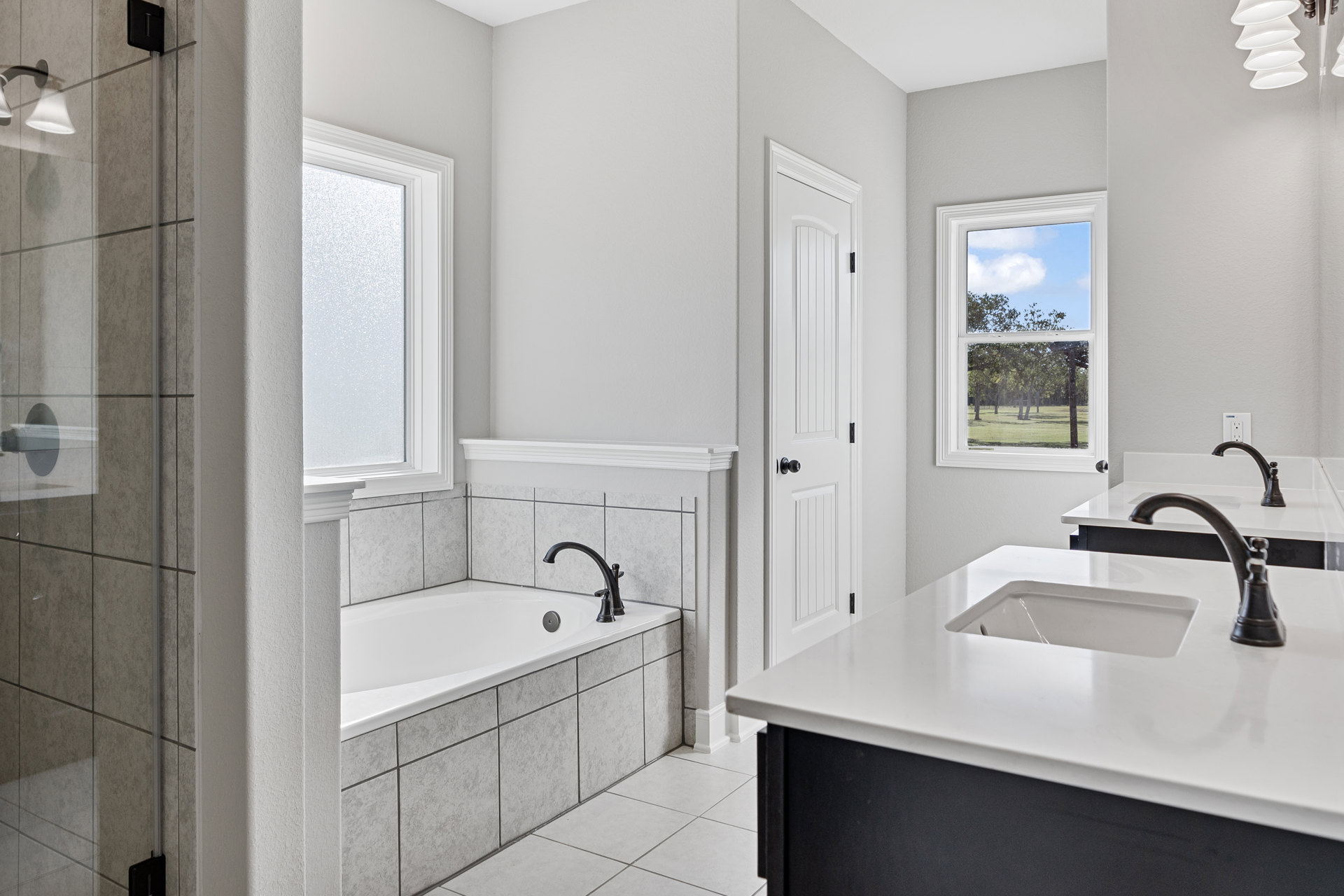 Modern bathroom featuring a freestanding white tub, white countertop with matte black faucet, rectangular window framing leafy trees, black vessel sink, and cluster of white