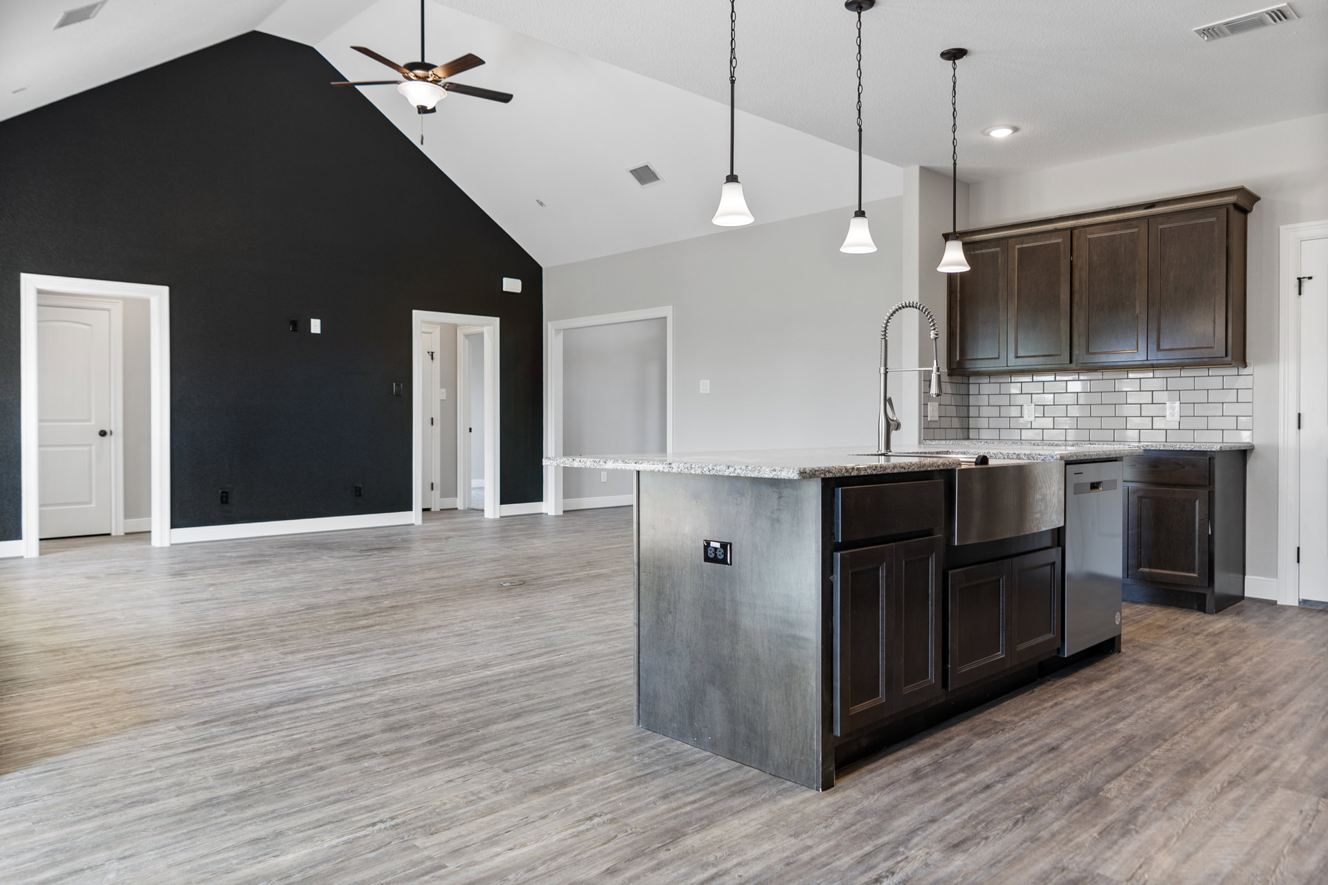 Spacious kitchen featuring a large central island with built-in sink and cabinetry, white door with black hardware, ceiling fan with light fixture, neutral walls and flooring