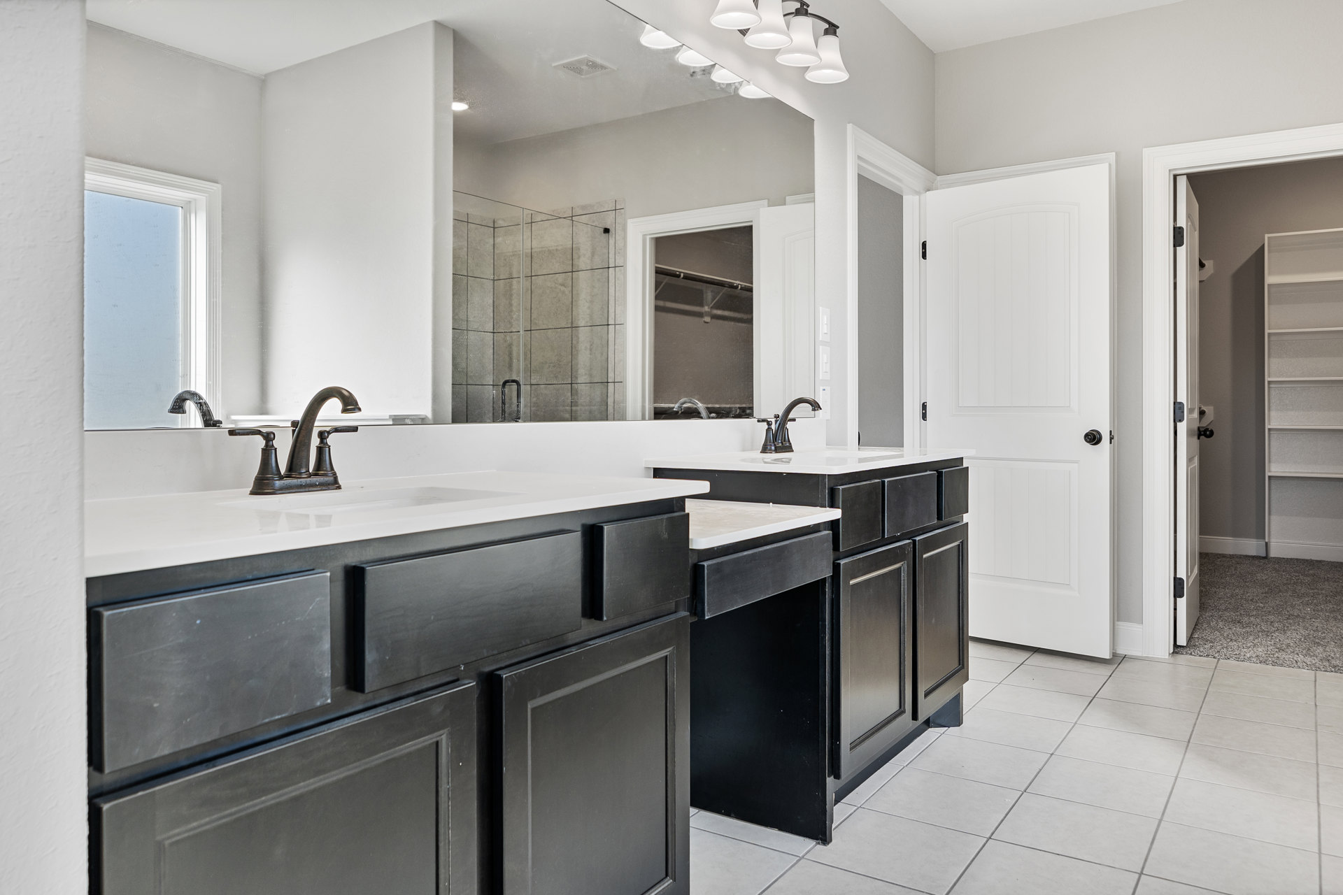 Black bathroom cabinets with white tile flooring, white sink and countertop, black cabinet hardware, white door with black knob, chrome faucet, white rectangular backsplash.
