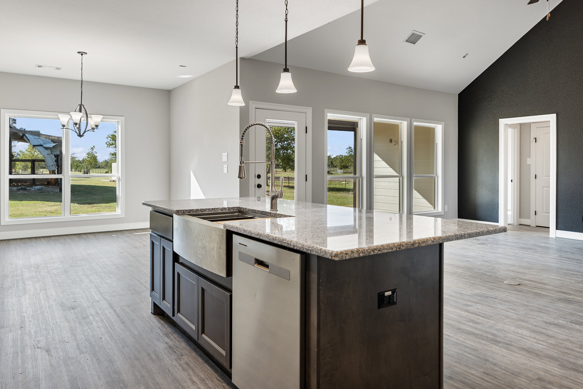 Spacious kitchen featuring a large central island with light stone countertop, white cabinetry, stainless steel sink, wood flooring, and recessed ceiling lights; black outlet with