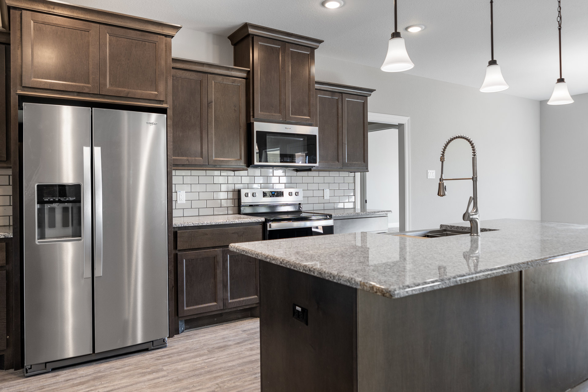Kitchen featuring stainless steel refrigerator with glass door, stainless steel island, built-in microwave, silver faucet with long handle, white cabinetry, and stone countertops
