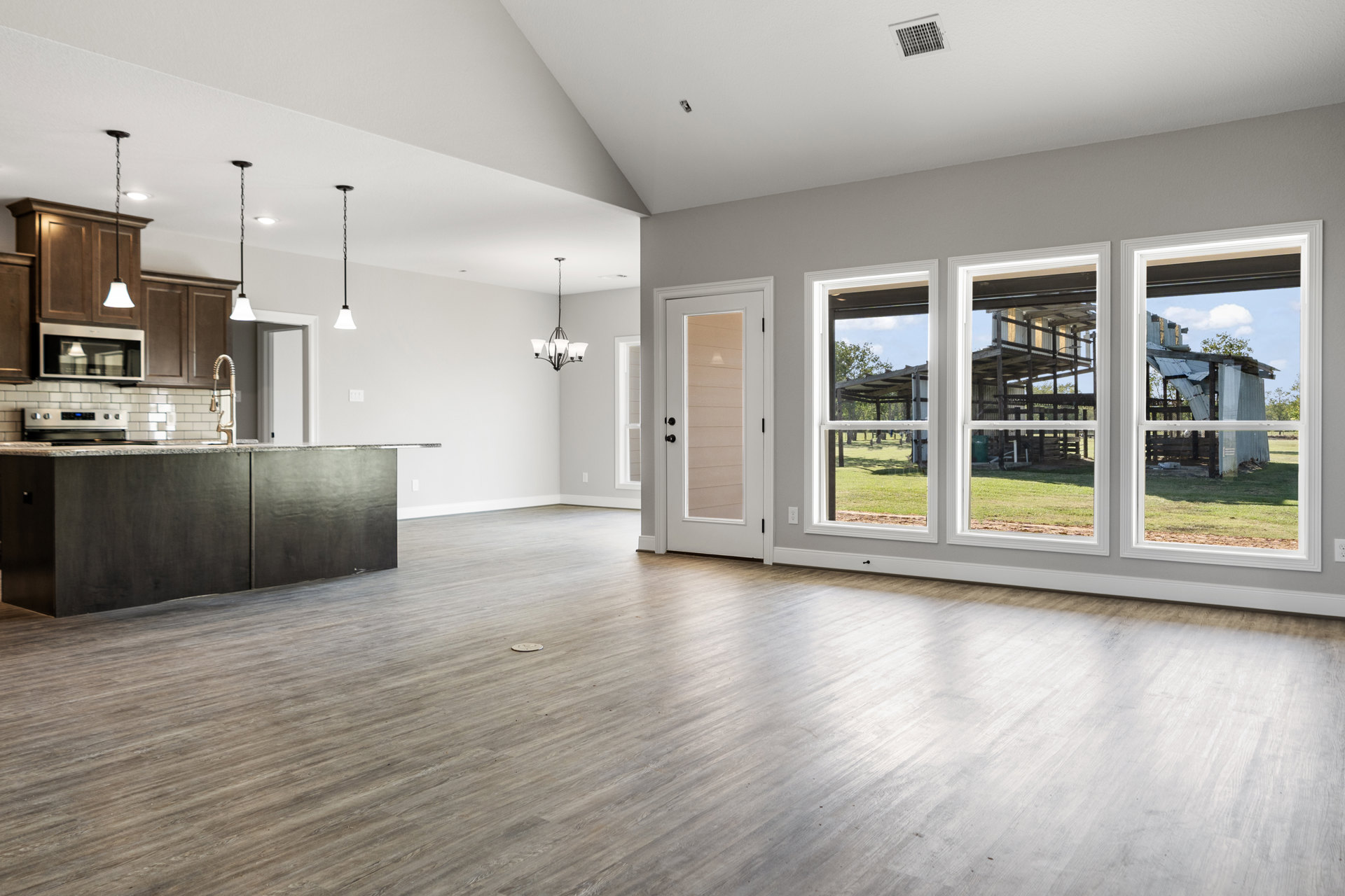 Spacious kitchen with wood flooring, white cabinetry, ceiling vent, glass panel door, and large window showing exterior building