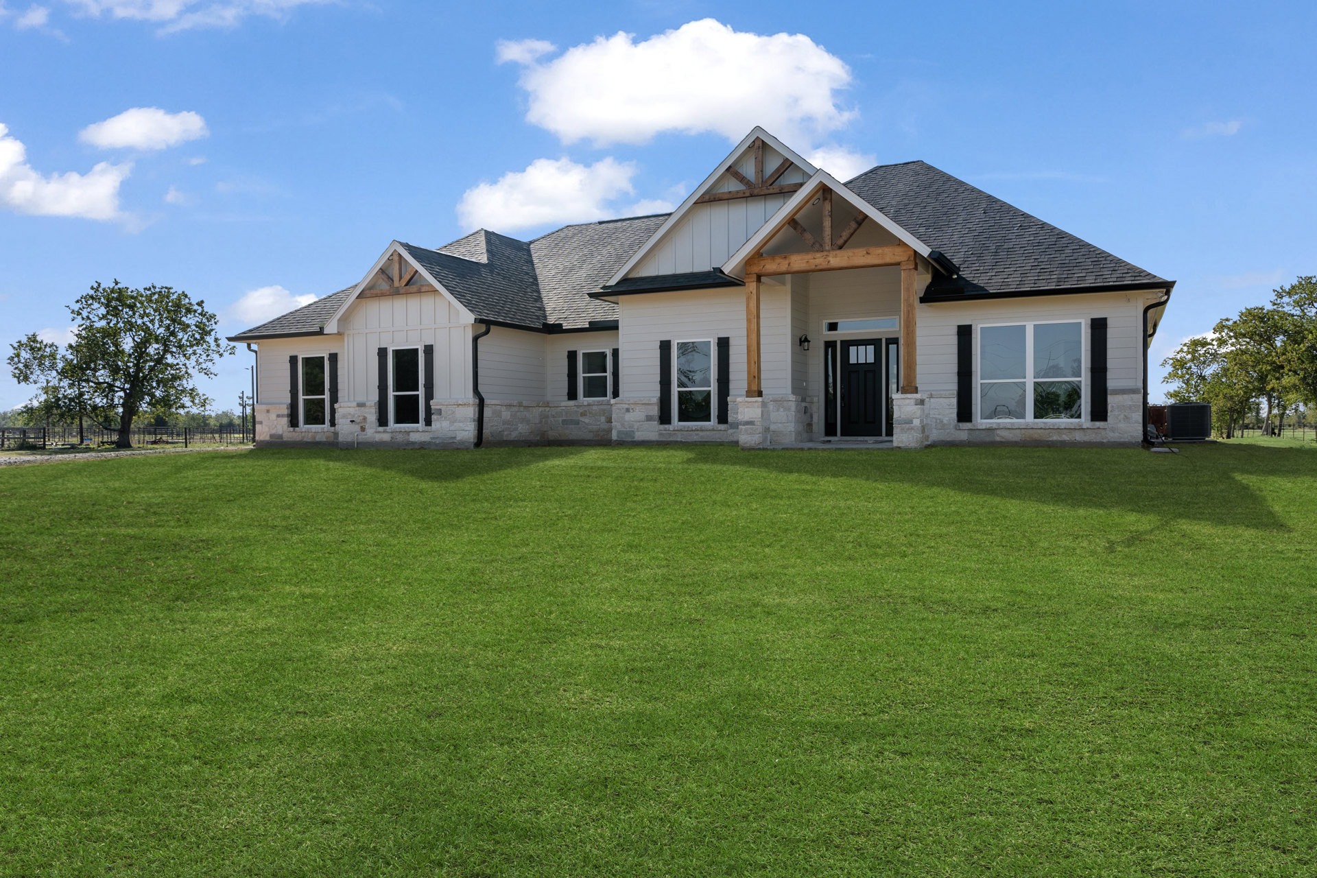 Modern home with black-framed windows and door, surrounded by a spacious green lawn, mature trees, and partly cloudy sky