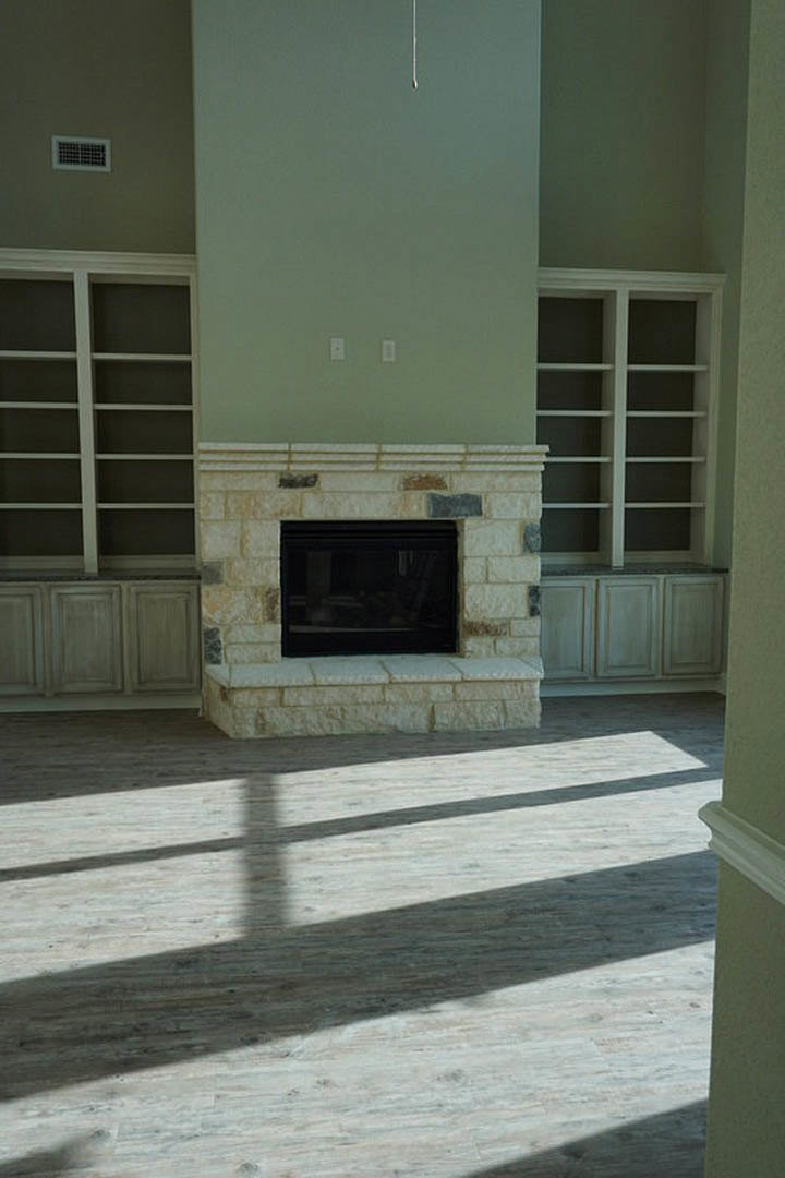 Stone fireplace with black frame set in a living room, flanked by white built-in shelves and light hardwood flooring.