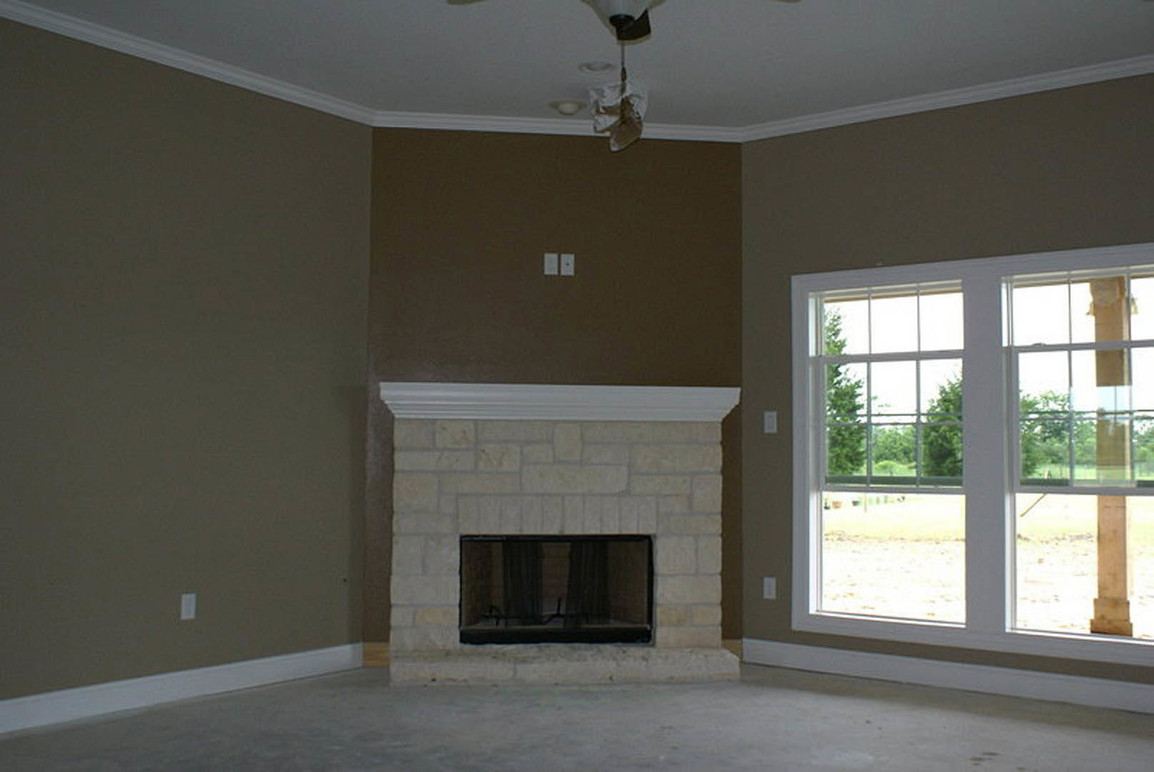 Brick fireplace set into plaster wall, concrete floor, black curtained window with tree view, ceiling light fixture, decorative molding