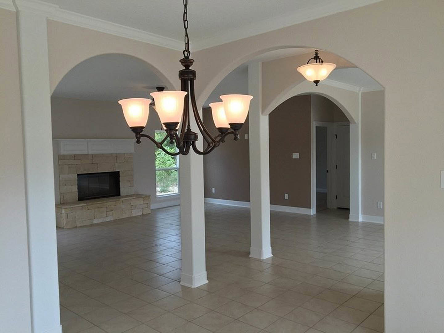 Chandelier with glass pendants hangs from white ceiling above tiled living room floor, flanked by white pillars and stone fireplace wall.