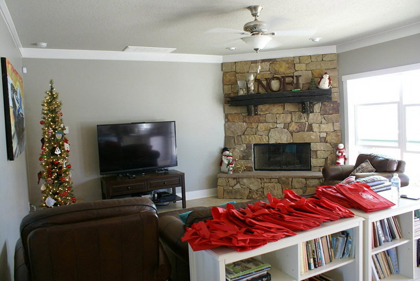 Living room with stone fireplace, decorated Christmas tree with lights and ornaments, gray sectional couch, wall-mounted black television, framed painting, built-in cabinetry