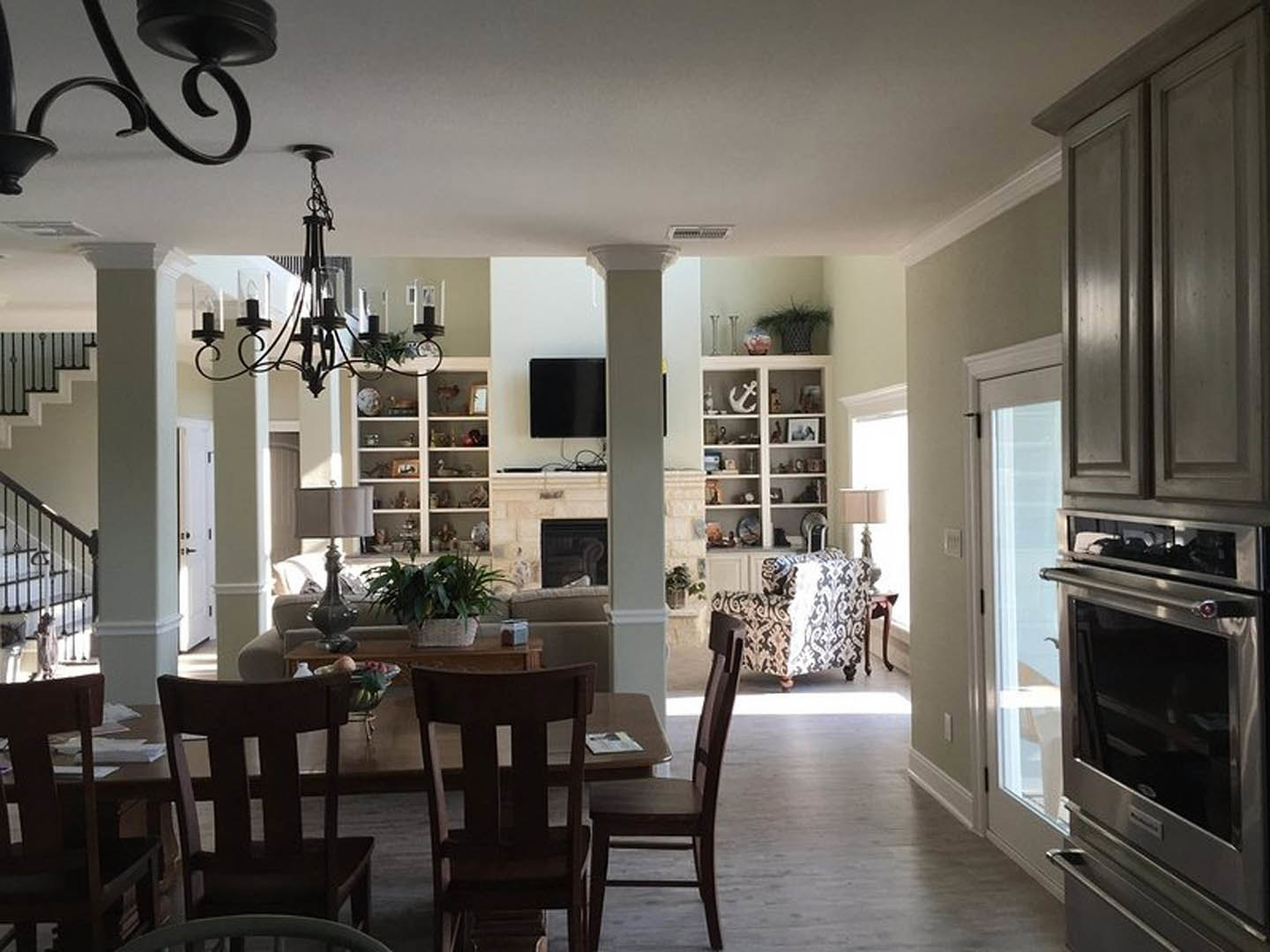 Living room with wood dining table and upholstered patterned chairs, potted plant on tabletop, built-in cabinetry, and partial view of kitchen appliances