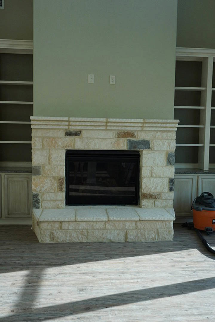 Modern gas fireplace with black glass surround set into a textured stone wall, white floating shelf above, dark accent background, hardwood flooring