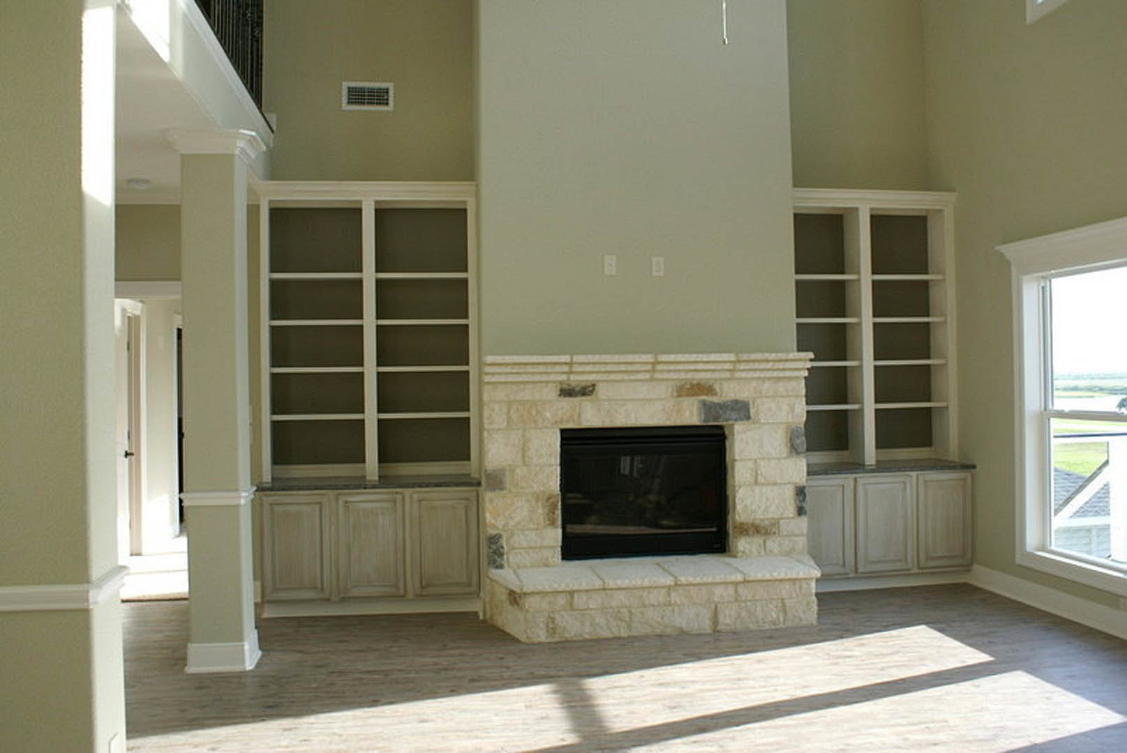 Modern living room with white walls, black-framed fireplace, wood flooring, large window, and decorative wall molding