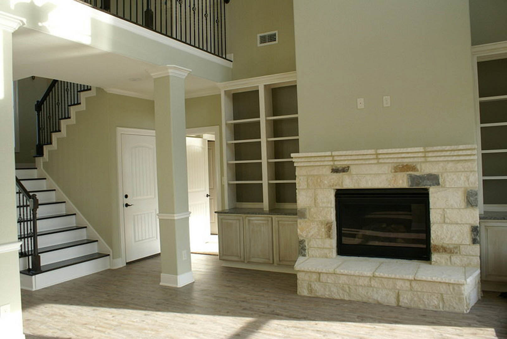 Living room featuring a stone fireplace, wood mantel, white pillar, hardwood floors, and staircase with white molding.