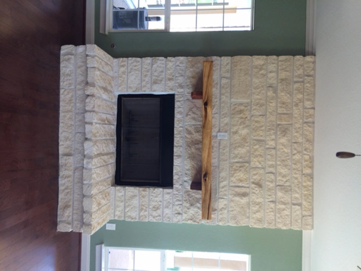 Modern living room with black rectangular fireplace framed by white surround, wood mantel shelf above, large window with white trim, light hardwood floors, and neutral painted