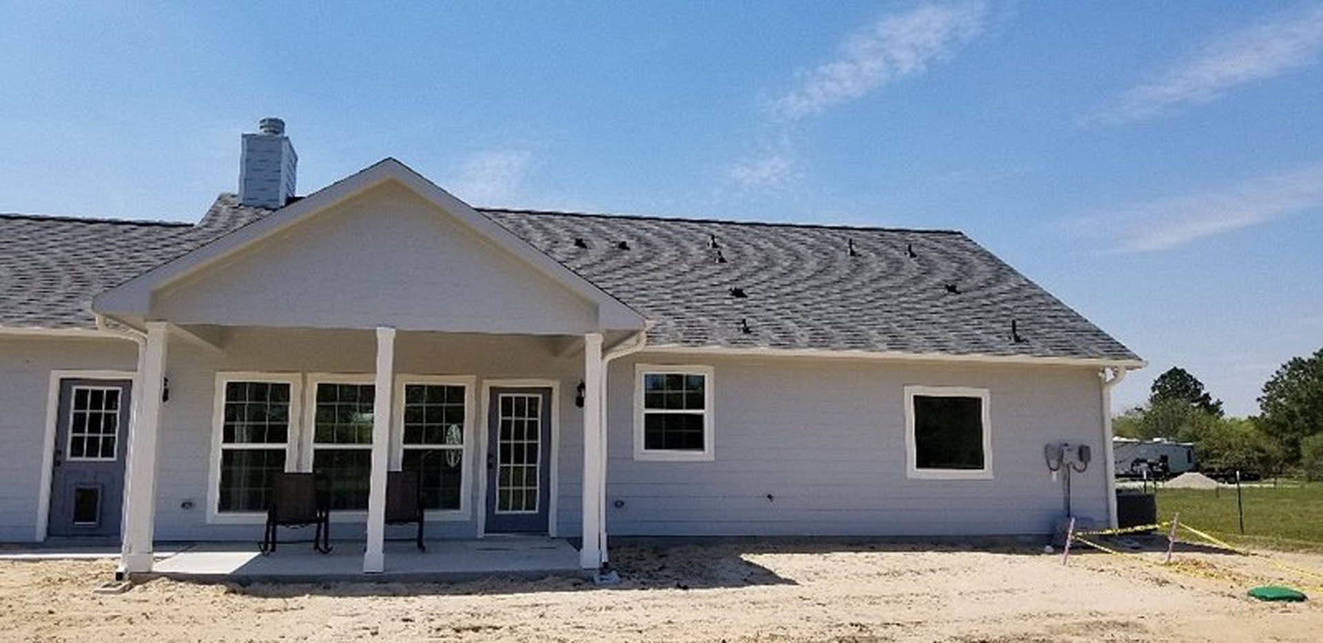 White clapboard house with covered front porch, wooden columns, dark framed windows, and a single chair near the entry door, set against a cloudy sky.