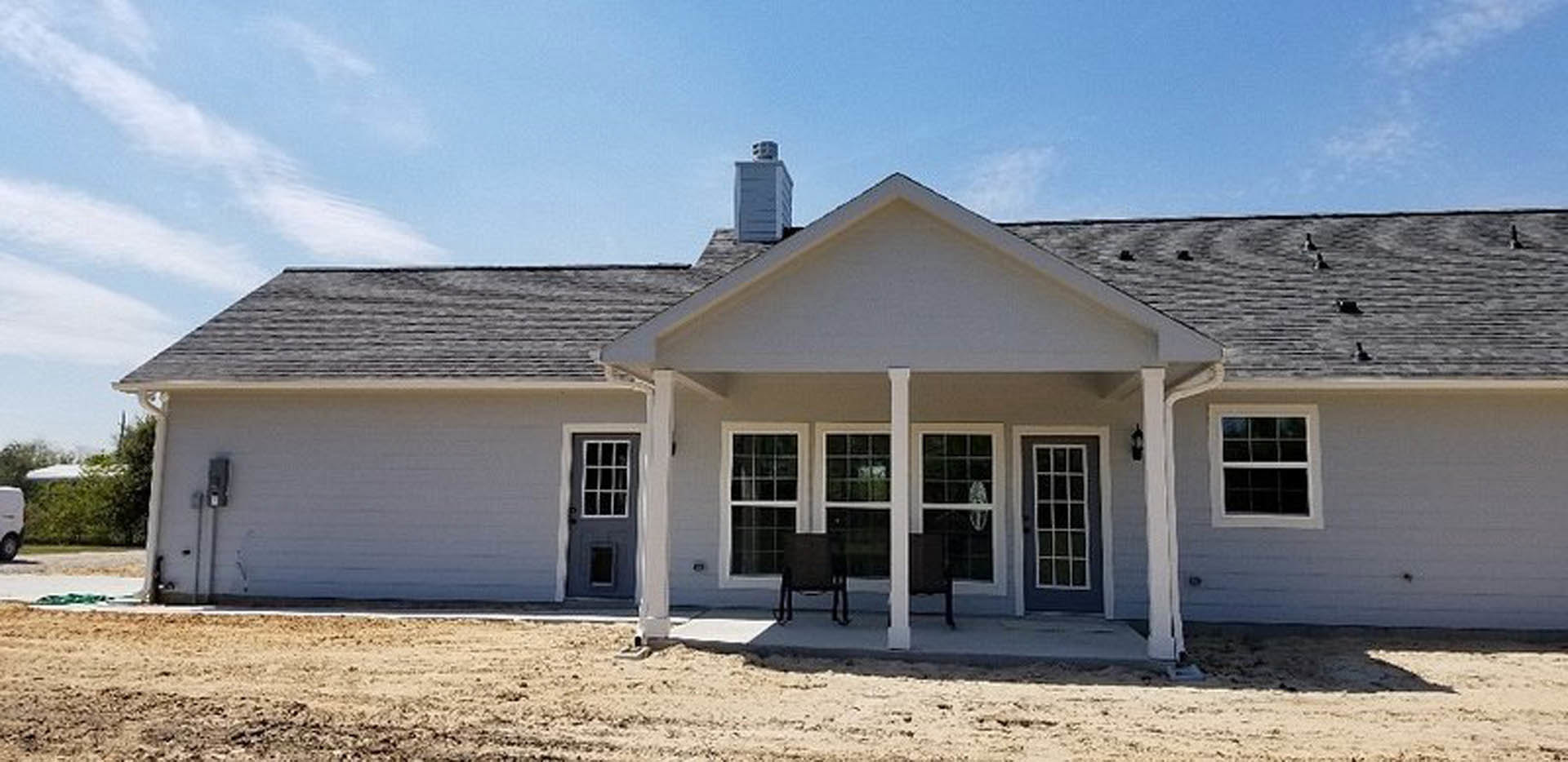 Two-story house with light siding, covered front porch, brick patio, large windows, and cloudy sky in background