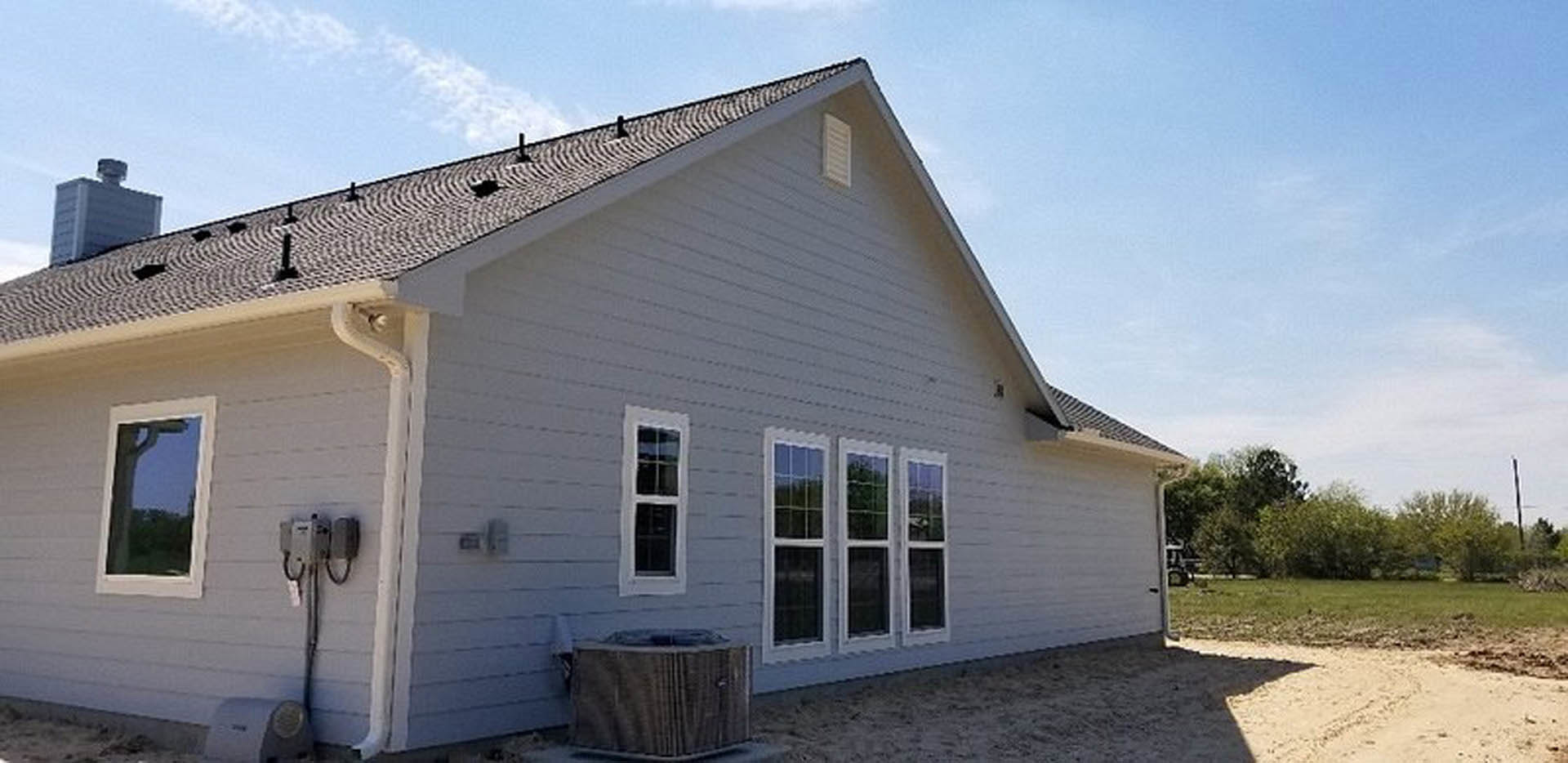 Two-story home with white siding, large front porch, multiple windows, expansive green lawn, and blue sky with scattered clouds
