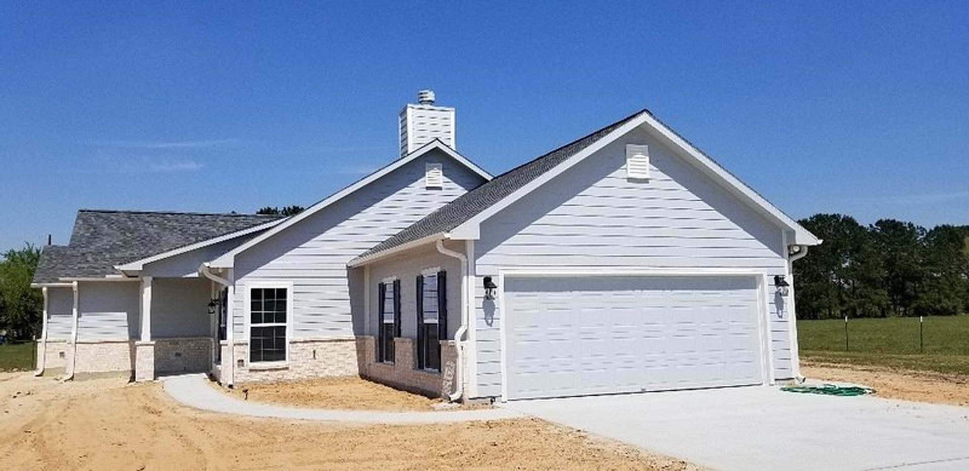 Gray siding house with attached garage, white-framed windows, shingled roof, and landscaped front yard under blue sky