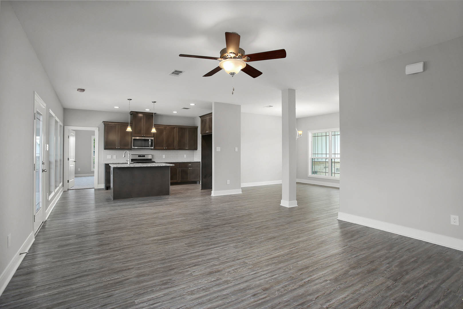 Open-concept kitchen with white cabinetry, stone countertops, hardwood flooring, ceiling fan with light fixture, and large window.