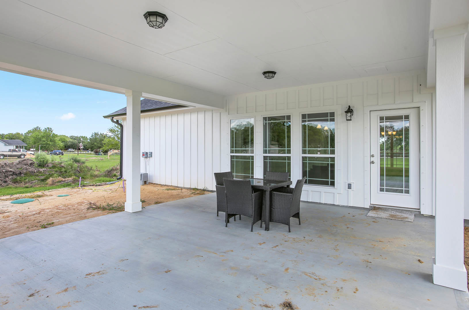 Concrete patio with metal chairs and a table, glass door entry, modern outdoor light fixture, blue sky in background
