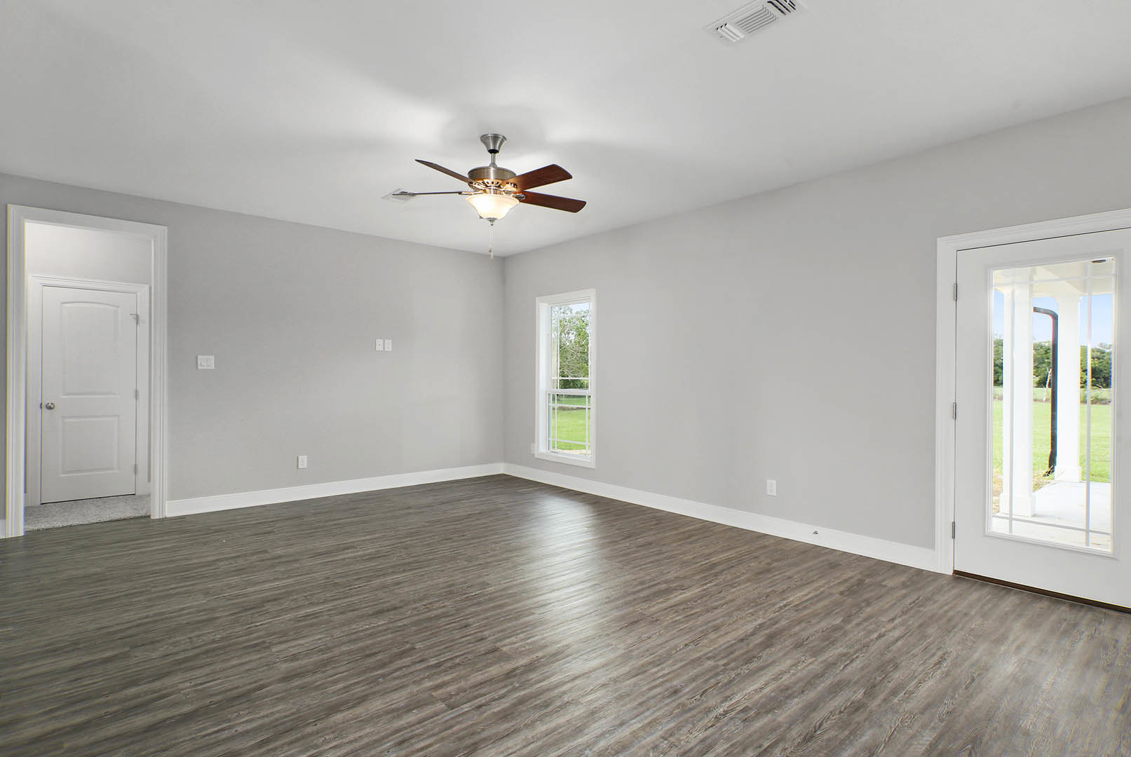 Room with wood laminate flooring, white walls, ceiling fan with light fixture, single window showing outdoor view, and white door with silver knob and black pipe.