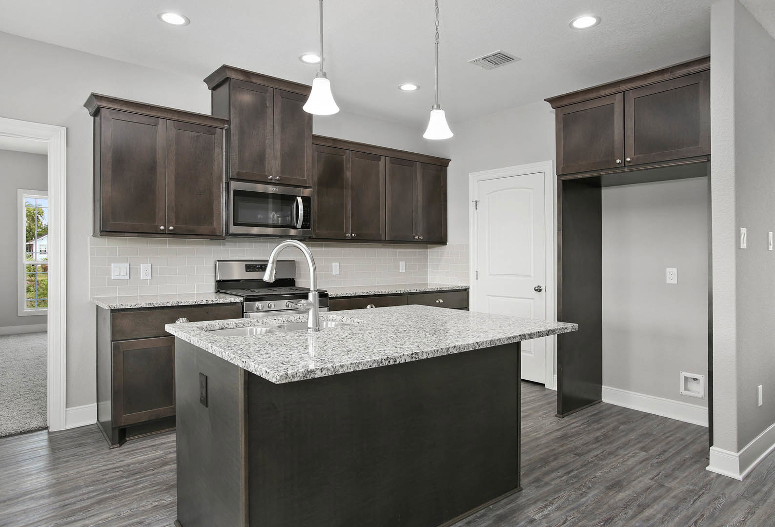 Marble kitchen island with built-in sink, white cabinetry, stainless steel microwave, pendant light fixture, window view of neighboring house and trees