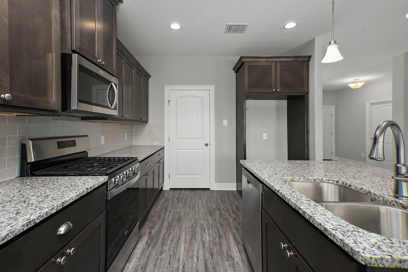 Granite countertops with tile backsplash, white cabinetry, stainless steel sink, stove and oven, white door with silver knob, built-in microwave, modern kitchen appliances