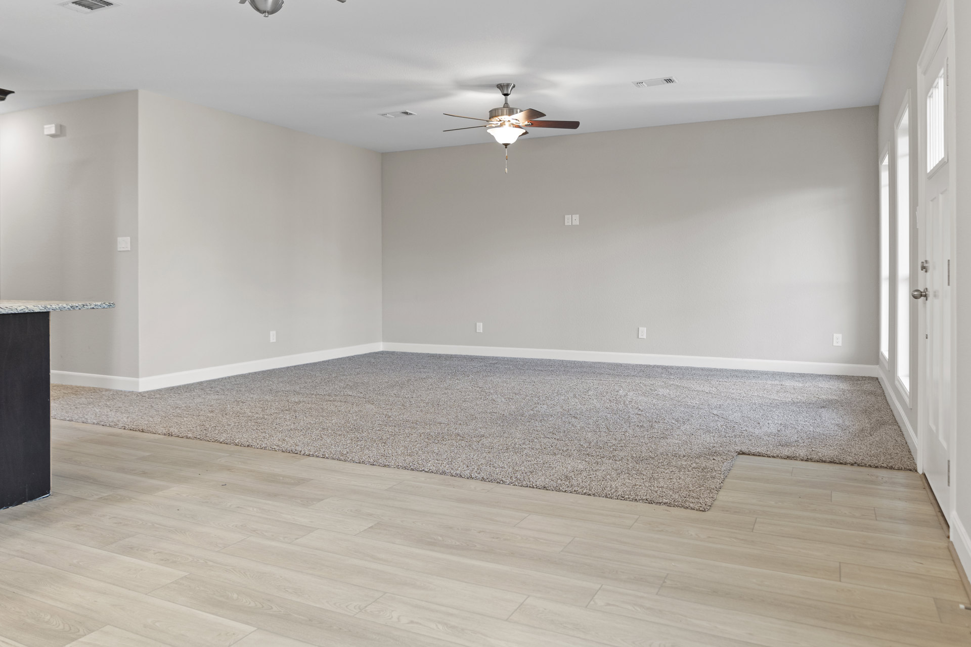 Neutral-toned carpeted room with white walls, ceiling fan featuring light fixture, and simple baseboards