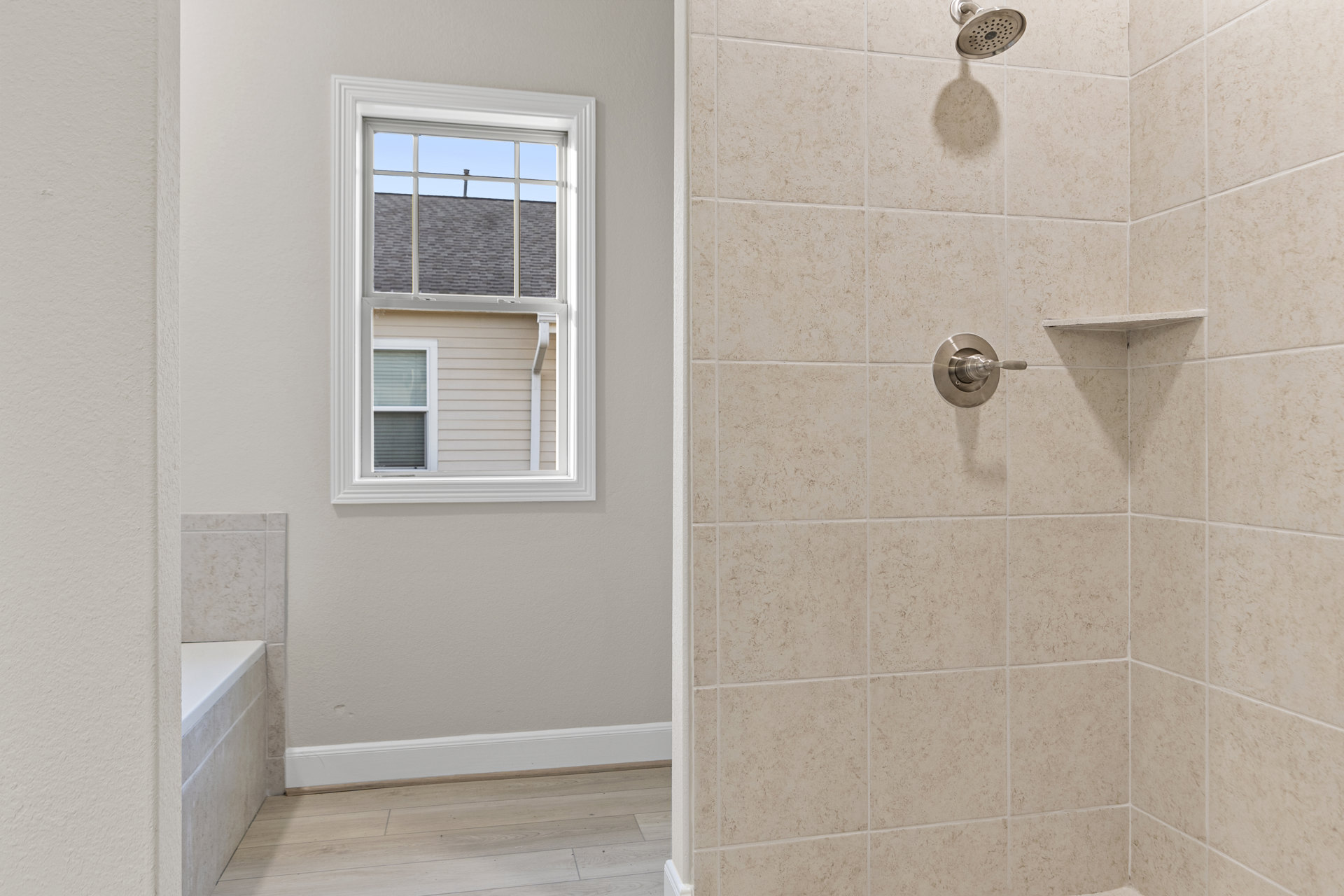 Walk-in shower with marble tile walls, glass enclosure, chrome shower head, and window letting in natural light; wood flooring transitions to white plaster wall outside shower